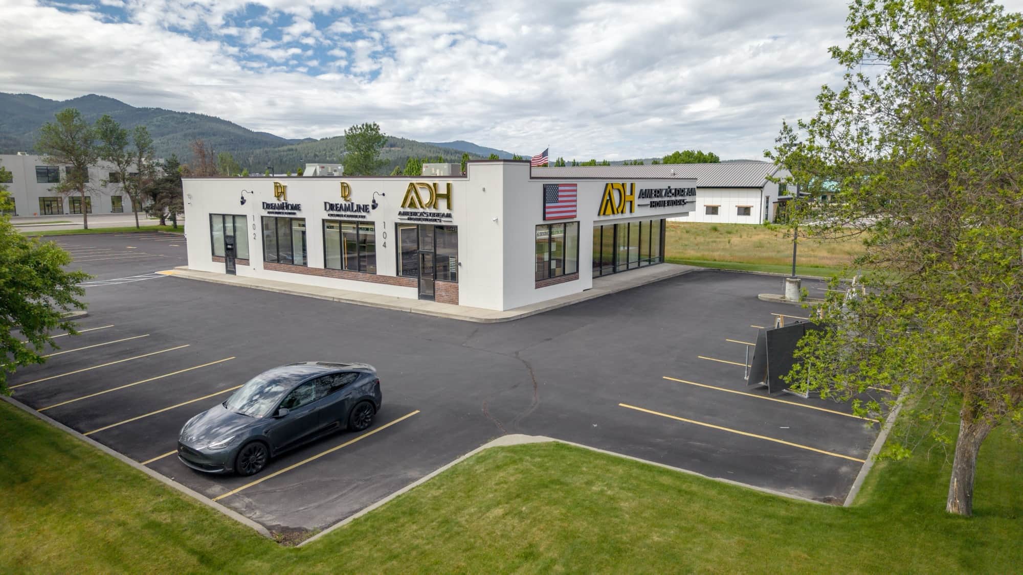 The single-story showroom building at 104 Moyie St in Post Falls seen across its parking lot, with glass suite entrances along the front elevation and forested hills behind