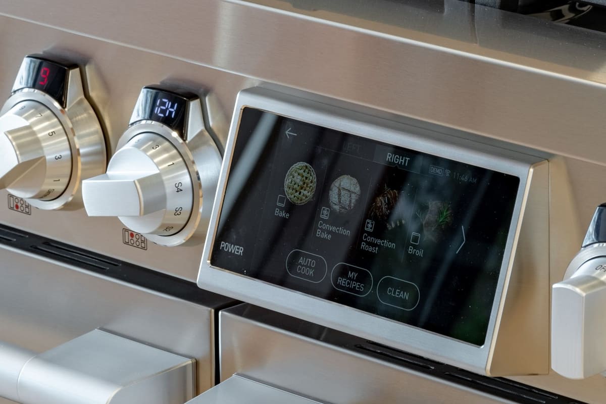 A professional range fascia with brushed steel control knobs and a lit touchscreen showing cooking modes